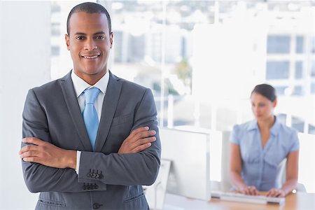 simsearch:400-07275828,k - Businessman standing with arms crossed with woman working behind Photographie de stock - Aubaine LD & Abonnement, Code: 400-06884398