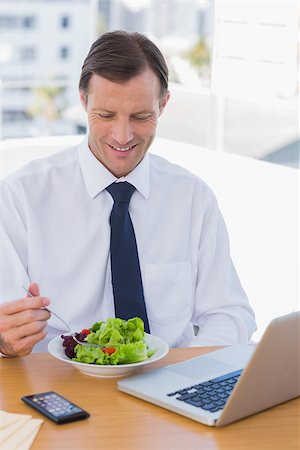 simsearch:400-06884500,k - Smiling businessman eating a salad on his desk during the lunch time Stock Photo - Budget Royalty-Free & Subscription, Code: 400-06884513