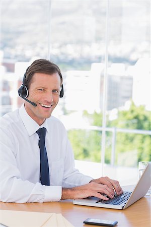 simsearch:400-06884500,k - Smiling businessman wearing a headset while using his laptop Stock Photo - Budget Royalty-Free & Subscription, Code: 400-06884530