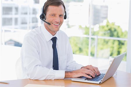 simsearch:400-06884500,k - Cheerful businessman wearing a headset while using his laptop Stock Photo - Budget Royalty-Free & Subscription, Code: 400-06884531
