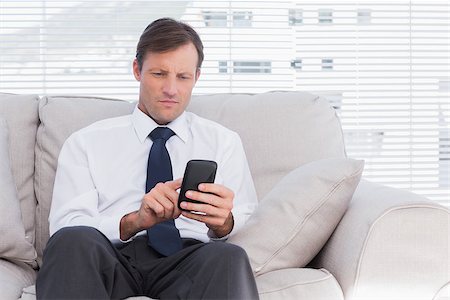 Businessman sitting on couch using his mobile phone Stock Photo - Budget Royalty-Free & Subscription, Code: 400-06884748