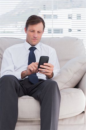 Attractive businessman typing text message and sitting on couch Stock Photo - Budget Royalty-Free & Subscription, Code: 400-06884749
