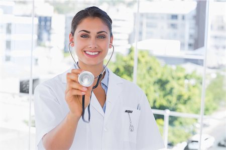 simsearch:400-06875982,k - Smiling young doctor holding up stethoscope to the camera Photographie de stock - Aubaine LD & Abonnement, Code: 400-06884855