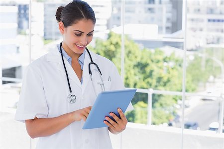 simsearch:400-06875998,k - Smiling young doctor using tablet pc by windows Photographie de stock - Aubaine LD & Abonnement, Code: 400-06884856