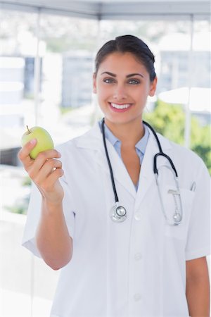 simsearch:400-06875982,k - Pretty young doctor holding a green apple and looking at camera Photographie de stock - Aubaine LD & Abonnement, Code: 400-06884860