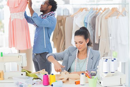simsearch:400-06885526,k - Fashion designer cutting textile at desk while her colleague adjusting dress behind Stock Photo - Budget Royalty-Free & Subscription, Code: 400-06885513