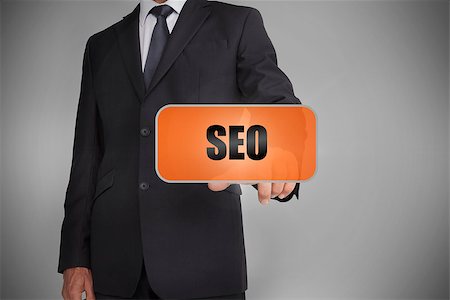 simsearch:400-06886051,k - Businessman touching orange tag with the word seo written on it on grey background Stock Photo - Budget Royalty-Free & Subscription, Code: 400-06885947