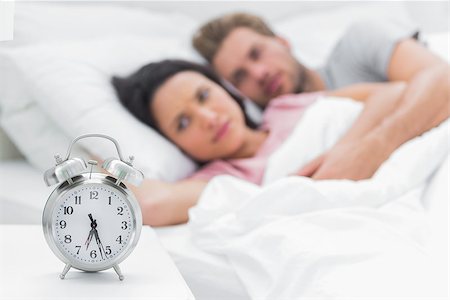 Tired couple looking at the alarm clock while they are in bed Stock Photo - Budget Royalty-Free & Subscription, Code: 400-06886254