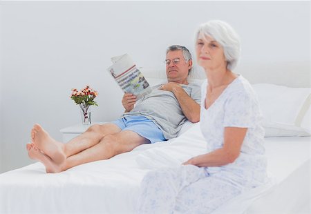 simsearch:400-06888132,k - Mature woman sitting on bed while husband is reading a newspaper on the background Photographie de stock - Aubaine LD & Abonnement, Code: 400-06888134