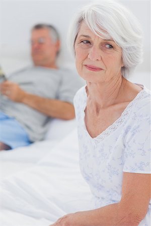 simsearch:400-06888132,k - Anxious mature woman sitting in bed while husband is reading a newspaper on the background Photographie de stock - Aubaine LD & Abonnement, Code: 400-06888137