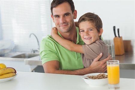 simsearch:400-06871178,k - Son embracing his father while having breakfast in the kitchen Stock Photo - Budget Royalty-Free & Subscription, Code: 400-06888458