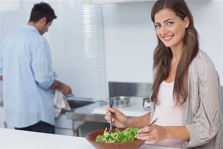 simsearch:6109-08488688,k - Woman mixing a salad in the kitchen while her husband is washing the dishes behind Stock Photo - Budget Royalty-Free & Subscription, Code: 400-06888617