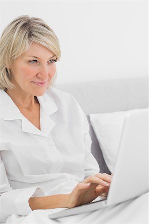 simsearch:400-06891122,k - Cheerful woman sitting in bed with laptop at home in bedroom Photographie de stock - Aubaine LD & Abonnement, Code: 400-06891099