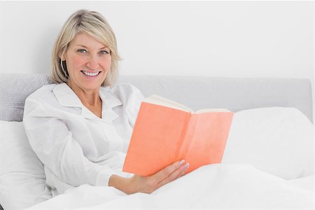 simsearch:400-06891126,k - Blonde woman sitting in bed reading smiling at camera at home in bedroom Stock Photo - Budget Royalty-Free & Subscription, Code: 400-06891105