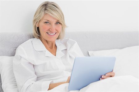 simsearch:400-06891126,k - Blonde woman sitting in bed using tablet pc smiling at camera at home Stock Photo - Budget Royalty-Free & Subscription, Code: 400-06891106