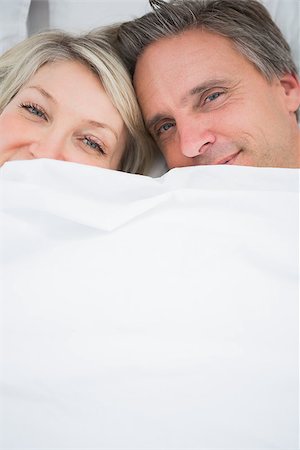 simsearch:400-06891126,k - Couple smiling at camera from under the covers at home in bed Stock Photo - Budget Royalty-Free & Subscription, Code: 400-06891126