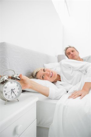 Blonde woman in bed with partner turning off alarm clock at home in bedroom Photographie de stock - Aubaine LD & Abonnement, Code: 400-06891141