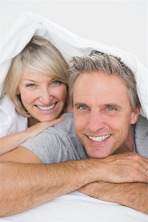 simsearch:400-06891122,k - Couple smiling under the covers at the camera at home in bed Photographie de stock - Aubaine LD & Abonnement, Code: 400-06891155