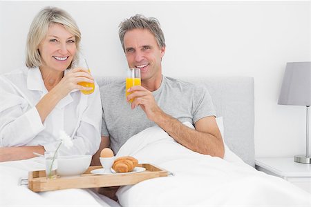 simsearch:400-06891122,k - Couple drinking orange juice at breakfast in bed smiling at the camera Photographie de stock - Aubaine LD & Abonnement, Code: 400-06891162