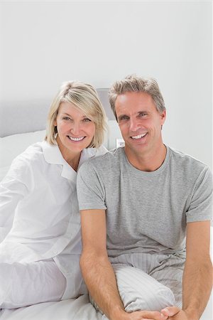 simsearch:400-06891122,k - Smiling couple sitting on bed looking at camera Photographie de stock - Aubaine LD & Abonnement, Code: 400-06891205