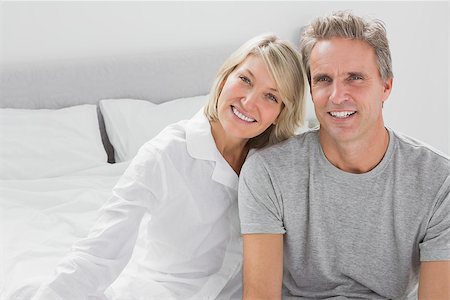 simsearch:400-06891126,k - Cheerful couple sitting on bed smiling at camera Stock Photo - Budget Royalty-Free & Subscription, Code: 400-06891206