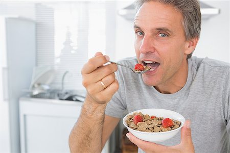 Happy man eating cereal for breakfast in kitchen looking at camera Stock Photo - Budget Royalty-Free & Subscription, Code: 400-06891224