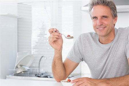 Happy man having cereal for breakfast in kitchen at home smiling at camera Stock Photo - Budget Royalty-Free & Subscription, Code: 400-06891221