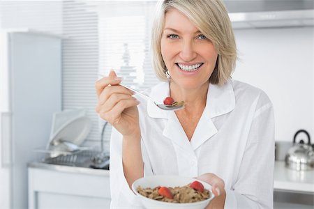 Cheerful blonde eating cereal for breakfast in kitchen looking at camera Stock Photo - Budget Royalty-Free & Subscription, Code: 400-06891243
