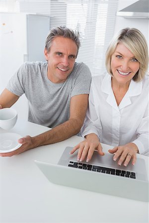 Cheerful couple using laptop in the morning looking at camera sitting at kitchen counter Stock Photo - Budget Royalty-Free & Subscription, Code: 400-06891256