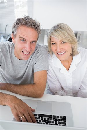 Smiling couple using their laptop in the morning looking at camera sitting at kitchen counter Stock Photo - Budget Royalty-Free & Subscription, Code: 400-06891262