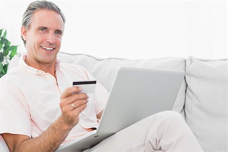 simsearch:400-07474252,k - Happy man on his couch using laptop for shopping online looking at camera Stock Photo - Budget Royalty-Free & Subscription, Code: 400-06891293