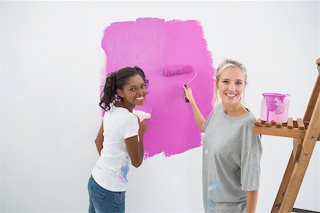 simsearch:400-07834992,k - Smiling young housemates painting wall pink in their new home looking at camera Fotografie stock - Microstock e Abbonamento, Codice: 400-06891529