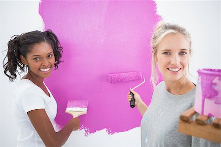 simsearch:400-07834992,k - Smiling housemates painting wall pink and looking at camera in new home Fotografie stock - Microstock e Abbonamento, Codice: 400-06891531