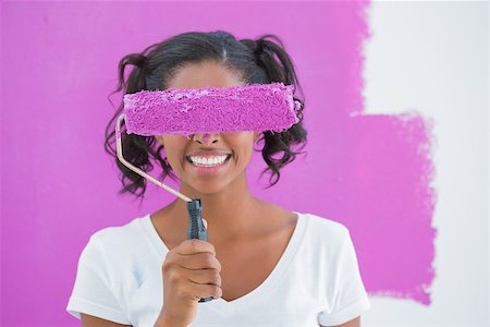 simsearch:400-07834992,k - Pretty woman holding paintroller over her face against a pink wall Fotografie stock - Microstock e Abbonamento, Codice: 400-06891555