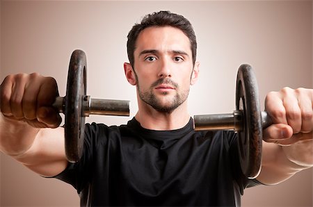 simsearch:400-06914161,k - Personal Trainer doing front dumbell raises for training his deltoids in a brown background Photographie de stock - Aubaine LD & Abonnement, Code: 400-06914116