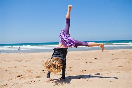 Cute young girl doing cartwheel in sand at beach with blue sky and ocean in background Foto de stock - Super Valor sin royalties y Suscripción, Código: 400-06917044