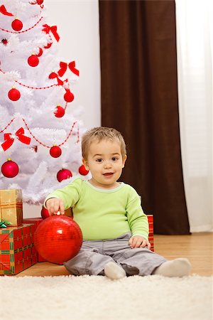 simsearch:400-04499150,k - Happy little boy sitting in front of Christmas tree, holding big red ornament Foto de stock - Royalty-Free Super Valor e Assinatura, Número: 400-06912561
