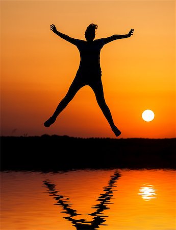 Silhouette woman jumping against orange sunset with reflection in water Stock Photo - Budget Royalty-Free & Subscription, Code: 400-06926810
