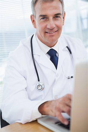 simsearch:614-06898452,k - Smiling experienced doctor typing on his laptop in bright office Stock Photo - Budget Royalty-Free & Subscription, Code: 400-06929947