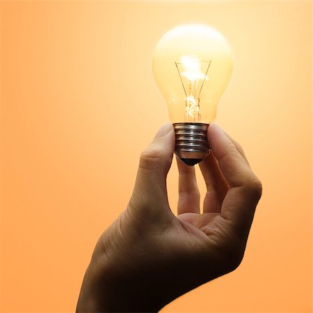 A luminescent light bulb hold by a human hand. Warm light. Foto de stock - Royalty-Free Super Valor e Assinatura, Número: 400-06921464