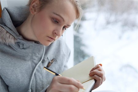 Young girl writing in her journal while sitting at a large window. Foto de stock - Royalty-Free Super Valor e Assinatura, Número: 400-06921760