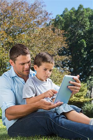 family with tablet in the park - Dad and son playing with a tablet PC in a park together on sunny day Photographie de stock - Aubaine LD & Abonnement, Code: 400-06934074