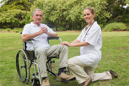 simsearch:6109-06684830,k - Cheerful man in a wheelchair with his nurse kneeling beside smiling at camera in the park Stock Photo - Budget Royalty-Free & Subscription, Code: 400-06934244