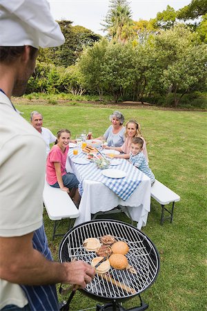Happy extended family having a barbecue being cooked by father in chefs hat outside in the sun Foto de stock - Super Valor sin royalties y Suscripción, Código: 400-06934305