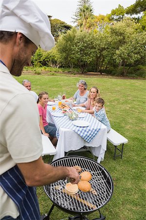 Smiling extended family having a barbecue being cooked by father in chefs hat outside in sunshine Stock Photo - Budget Royalty-Free & Subscription, Code: 400-06934306