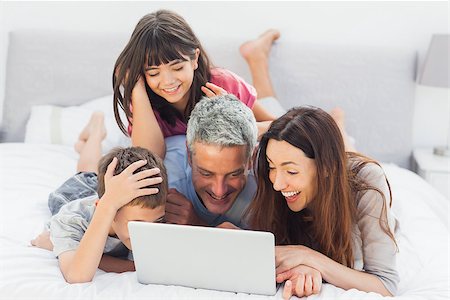 simsearch:400-06930138,k - Smiling family lying on bed using their laptop at home Stock Photo - Budget Royalty-Free & Subscription, Code: 400-06930085
