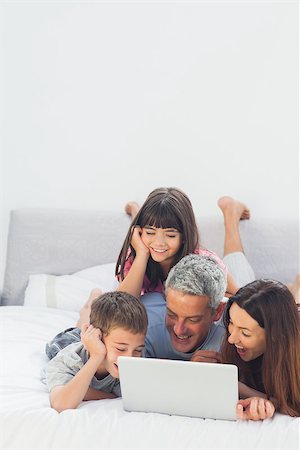 simsearch:400-06930138,k - Happy family lying on bed using their laptop at home Stock Photo - Budget Royalty-Free & Subscription, Code: 400-06930086