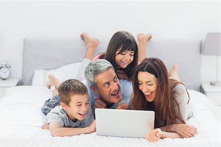simsearch:400-06930138,k - Cheerful family lying on bed using their laptop at home Stock Photo - Budget Royalty-Free & Subscription, Code: 400-06930087
