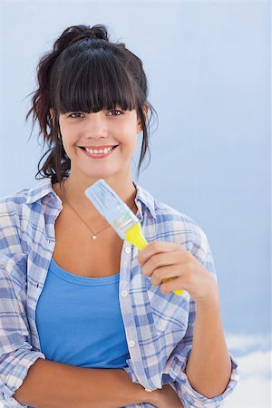 Pretty woman holding paint brush smiling at camera against a blue wall Photographie de stock - Aubaine LD & Abonnement, Code: 400-06931055