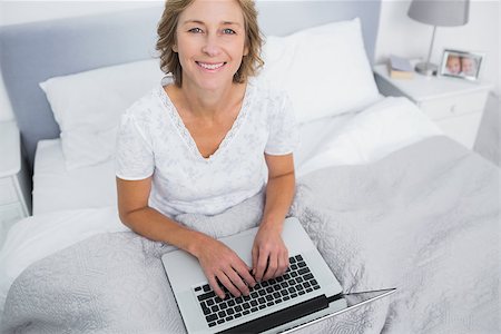 Smiling blonde woman in bed using her laptop looking at camera in bedroom at home Stock Photo - Budget Royalty-Free & Subscription, Code: 400-06931196